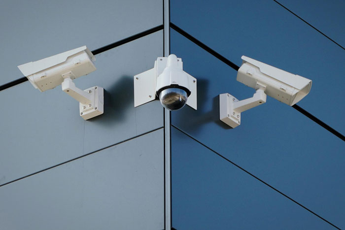 Three security cameras mounted on the corner of a modern glass building monitoring family safety and parole compliance.