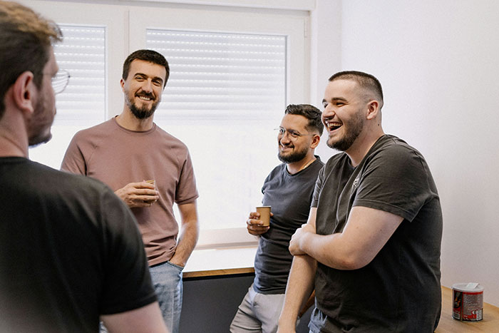Group of men laughing and talking indoors, illustrating a restaurant pitching idea after a snarky letter leads to a patent opportunity.