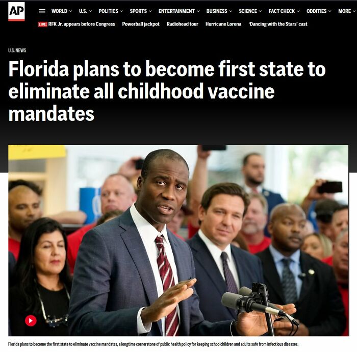 Politician speaking at press conference about childhood vaccine mandates with people listening in the background.