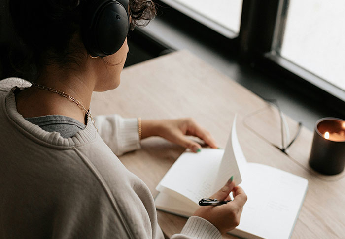 Person wearing headphones and reading a book by the window, focusing on skills to improve life and retire rich.