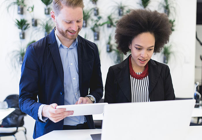 Two professionals collaborating on a laptop and tablet, focusing on easy skills to improve life and retire rich.