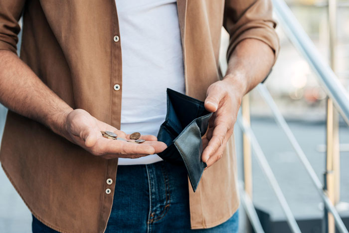 Unemployed guy holding empty wallet and loose coins, wearing brown shirt and jeans on outdoor steps Unemployed guy holding empty wallet and loose coins, wearing brown shirt and jeans on outdoor steps