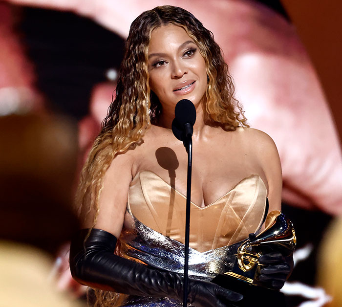 Beyonc&eacute; holding a Grammy award while speaking at a microphone, illustrating Grammy snubs impact on fans.
