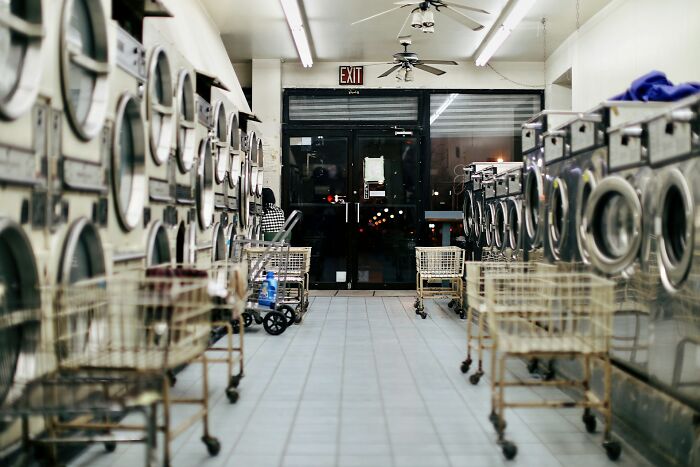 Empty laundromat interior with rows of washing machines and laundry carts, illustrating weird public moments without shame.
