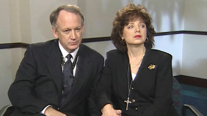 Two serious people in formal attire seated indoors, related to biggest unsolved cases from all over the world.