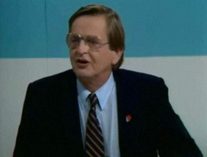 Man in suit and glasses speaking during a formal event, related to the biggest unsolved cases worldwide.