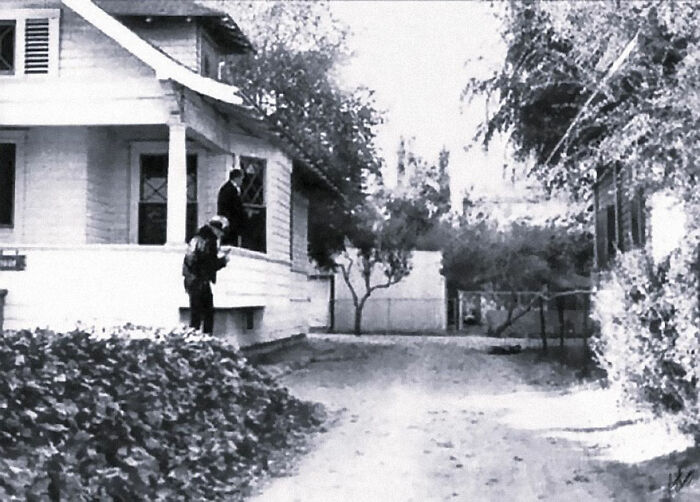 Black and white photo of investigators examining the exterior of a residential house in one of the biggest unsolved cases.