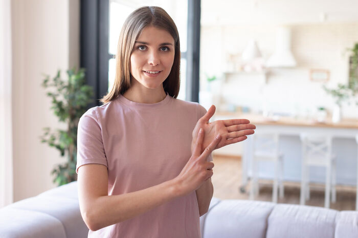 Young woman in pink shirt at home, looking confident while illustrating a point in a casual setting for bilingual stories.