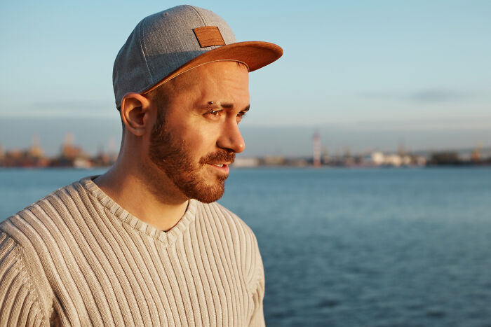 Young man in a cap near water, reflecting on awkward moments bilingual people caught gossiping about them.