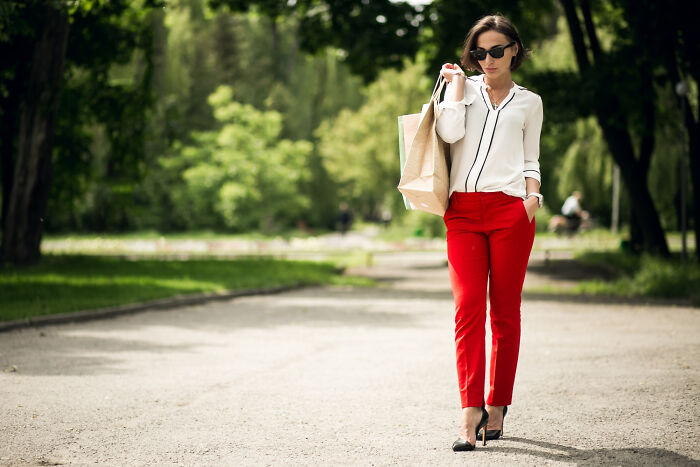 Woman in sunglasses and red pants walking outdoors, symbolizing awkward bilingual gossip moments caught.