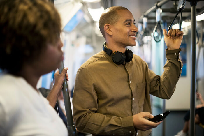 Bilingual man on public transit catching someone gossiping about him with headphones around his neck.