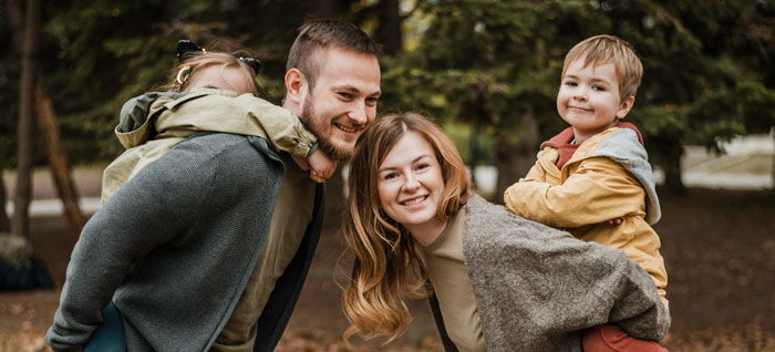 Happy teenage family spending time outdoors with children playing piggyback, representing teen refusing to live with bio parents.