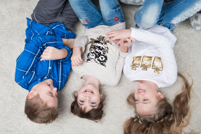 Three children lying on carpet, smiling and holding hands, illustrating teen refuses to live with bio parents dispute.
