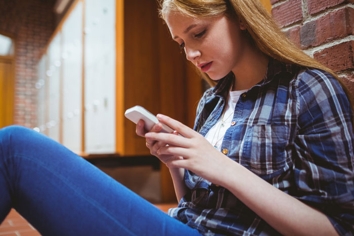Teen girl sitting against a brick wall, looking at phone, reflecting feelings of bio mom reappearing after 16 years hurt Teen girl sitting against a brick wall, looking at phone, reflecting feelings of bio mom reappearing after 16 years hurt