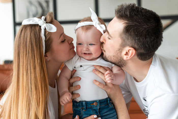 Young parents kissing their smiling baby girl, highlighting bio mom appears after 16 years in family reunion moment. Young parents kissing their smiling baby girl, highlighting bio mom appears after 16 years in family reunion moment.