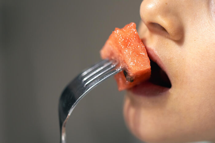 Close-up of person eating watermelon with a fork, illustrating unusual local delicacies and bizarre food choices.