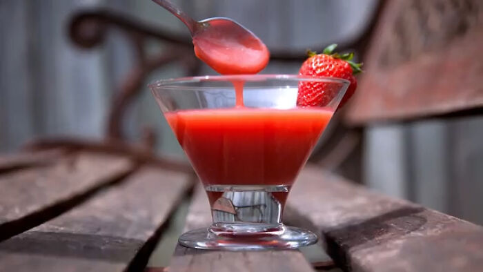Glass of red local delicacy sauce with a spoon and fresh strawberry on a rustic wooden bench outdoors