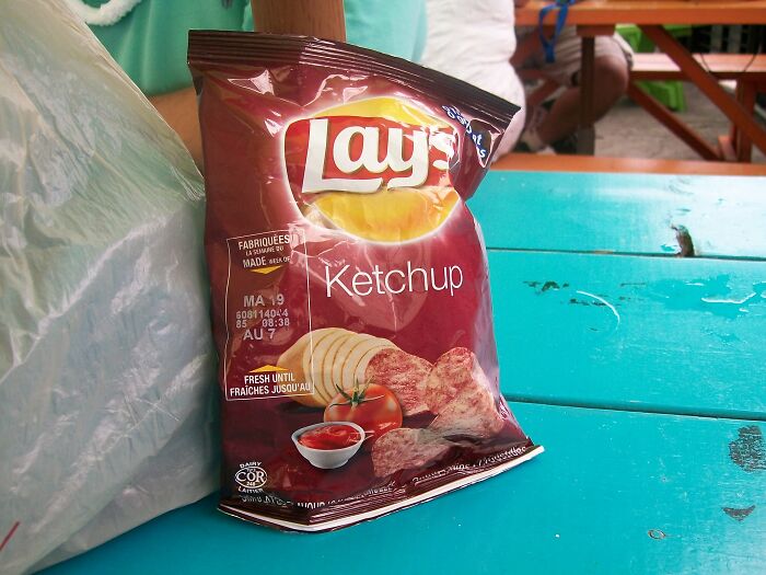 A bag of Lay’s Ketchup flavored chips on a blue wooden picnic table, representing unusual local delicacies.