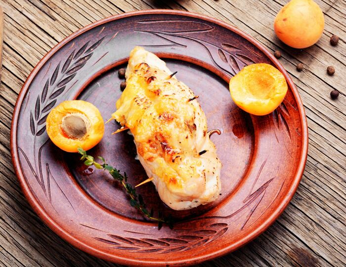 Grilled unusual local delicacy on a wooden plate with apricot halves and herbs, showcasing exotic food culture.