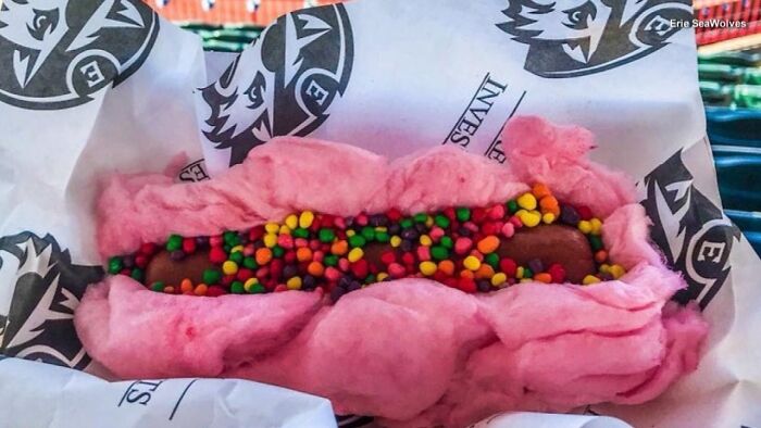 Pink cotton candy wrapped hot dog topped with colorful candy sprinkles, an unusual disgusting local delicacy food item.