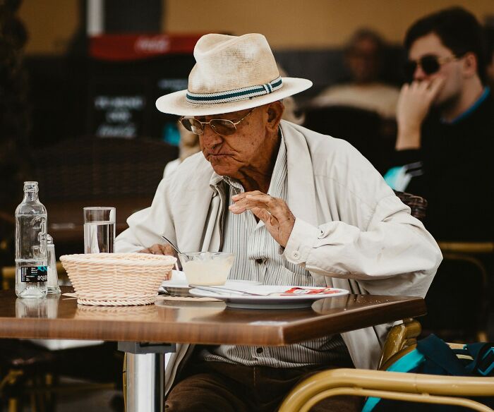 Elderly man in a hat eating at an outdoor cafe, depicting awkward moments people in the service industry face.