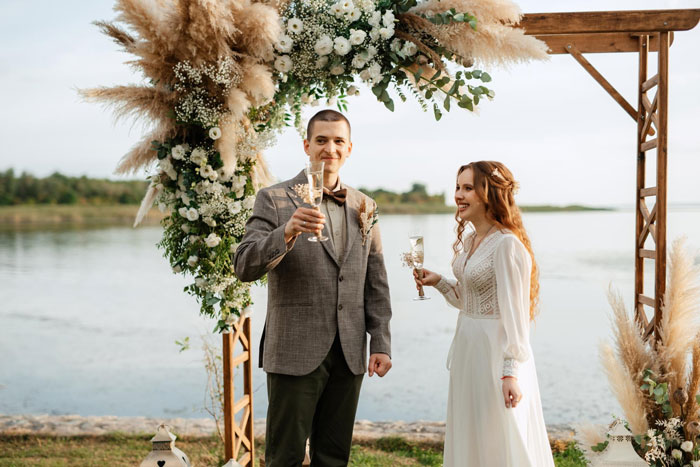 Couple celebrating wedding day under floral arch by the water, highlighting ownership clash over wedding date conflict.