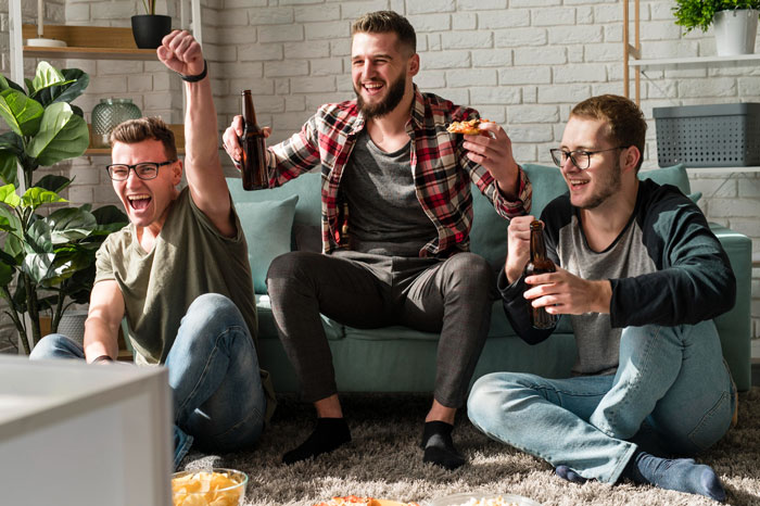 Three men cheering with beers and pizza in a living room, boyfriend ban friends relationship topic Three men cheering with beers and pizza in a living room, boyfriend ban friends relationship topic