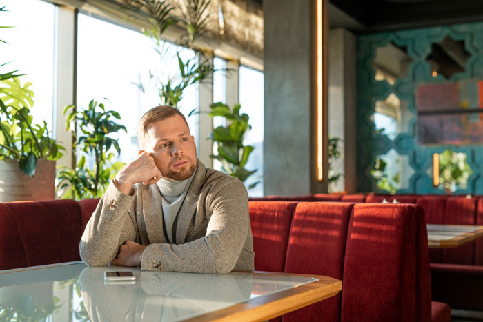 Man reflecting alone in a cafe, appearing thoughtful after a teenage bullying incident and relationship fallout. Man reflecting alone in a cafe, appearing thoughtful after a teenage bullying incident and relationship fallout.
