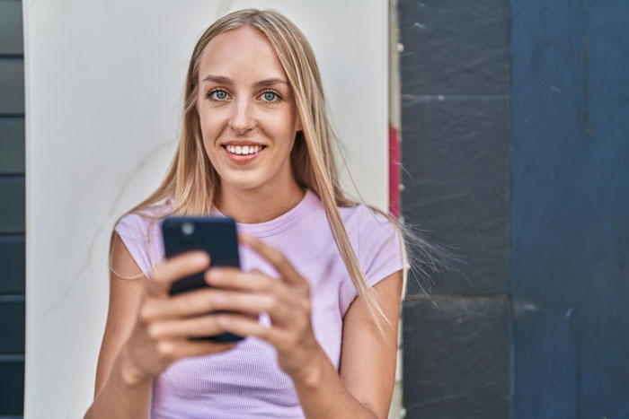 Young woman smiling while holding a smartphone, illustrating the theme of a girlfriend's uno-reverse breakup on birthday.