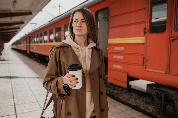 Woman holding coffee cup standing by a red train at the station, reflecting on bullying and relationship reversal. Woman holding coffee cup standing by a red train at the station, reflecting on bullying and relationship reversal.