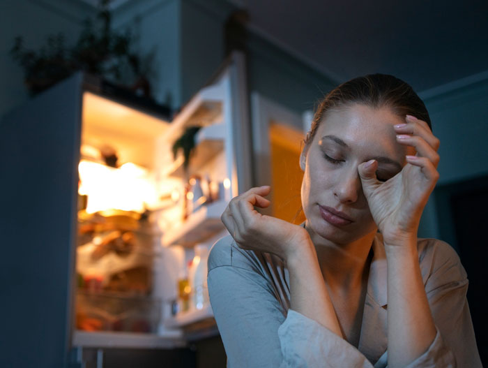 Woman sitting tired and stressed in front of an open fridge, triggered by childhood trauma during Christmas tradition. Woman sitting tired and stressed in front of an open fridge, triggered by childhood trauma during Christmas tradition.