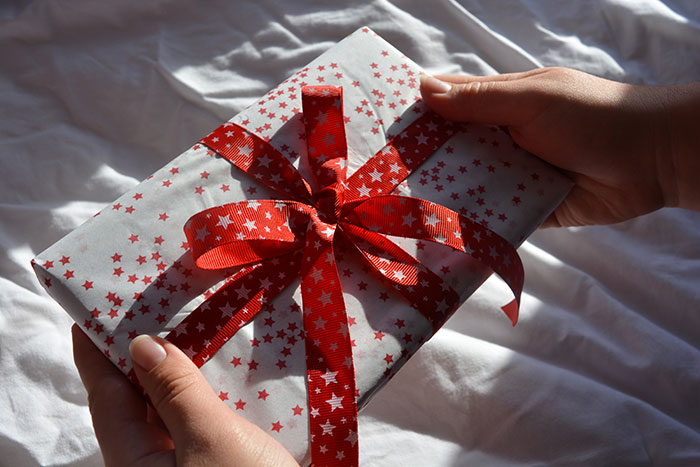 Hands holding a wrapped Christmas present with red star pattern and ribbon, related to man failing to buy holiday gifts. Hands holding a wrapped Christmas present with red star pattern and ribbon, related to man failing to buy holiday gifts.
