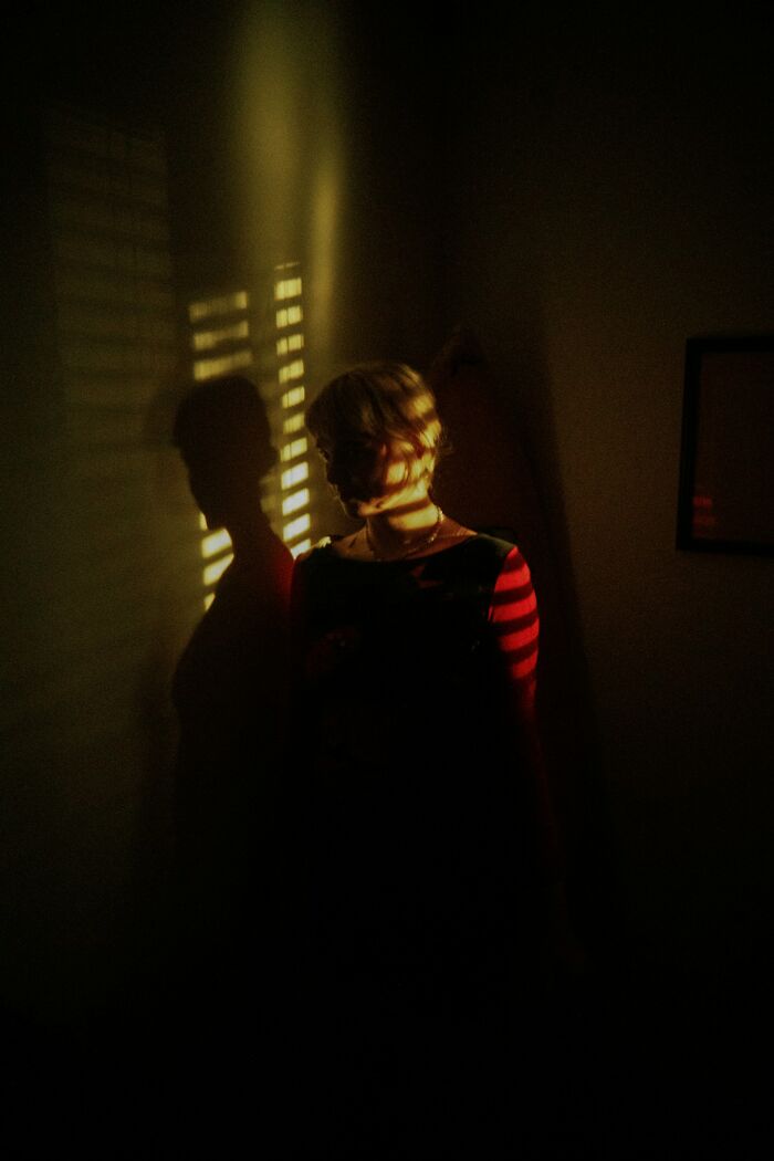 Person standing in dark room with striped shadow on face and wall, capturing terrifying real-life moments ambiance.