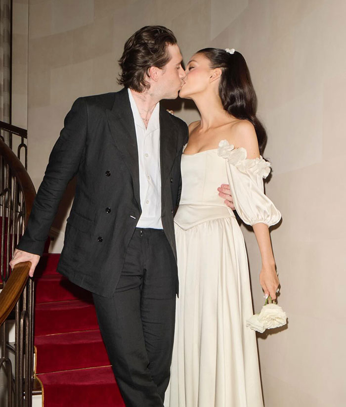 Brooklyn Beckham kissing his partner on a staircase, dressed formally amid discussions of family feud and being out of touch