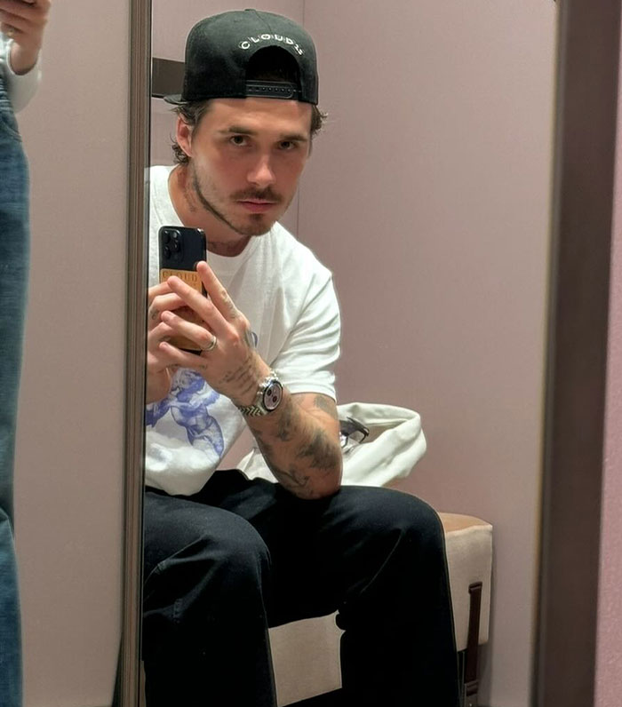 Brooklyn Beckham taking a mirror selfie wearing a cap and casual clothes amid family feud social media posts.