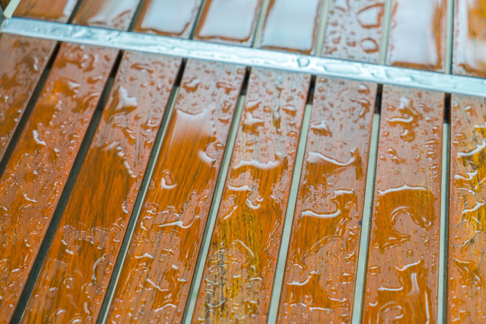 Close-up of a wet wooden surface with water droplets highlighting stains and grime on the slatted wood.