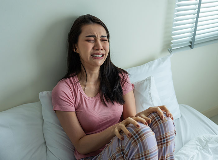 Woman sitting on bed crying and distressed, depicting emotional impact of brother's stalker tendencies in a home setting.