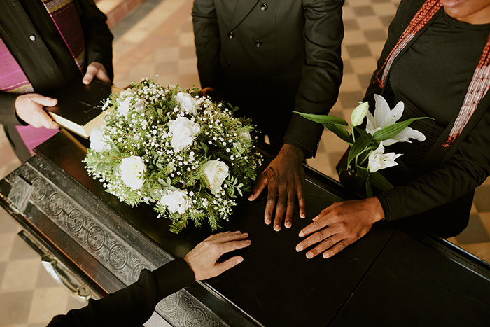 Mourning hands resting on a casket with white flowers, symbolizing loss and distress caused by family stalking.