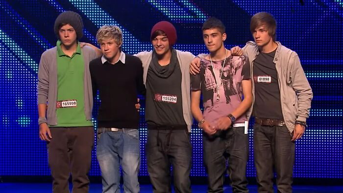 Boy band standing together on stage during a talent show audition, representing celebs who weren’t nepo babies.