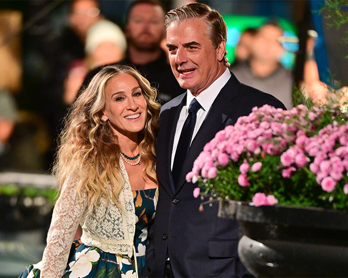 Chris Noth and Sarah Jessica Parker attending an event with flowers in the foreground and blurred crowd background.