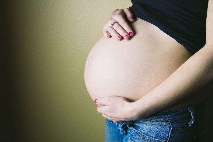 Pregnant woman holding belly wearing jeans and a black top, representing adult goals in life.