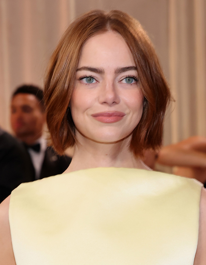 Young woman with glowing skin and red hair smiling at an event, showcasing celebrity facialist secrets for Golden Globes glow.