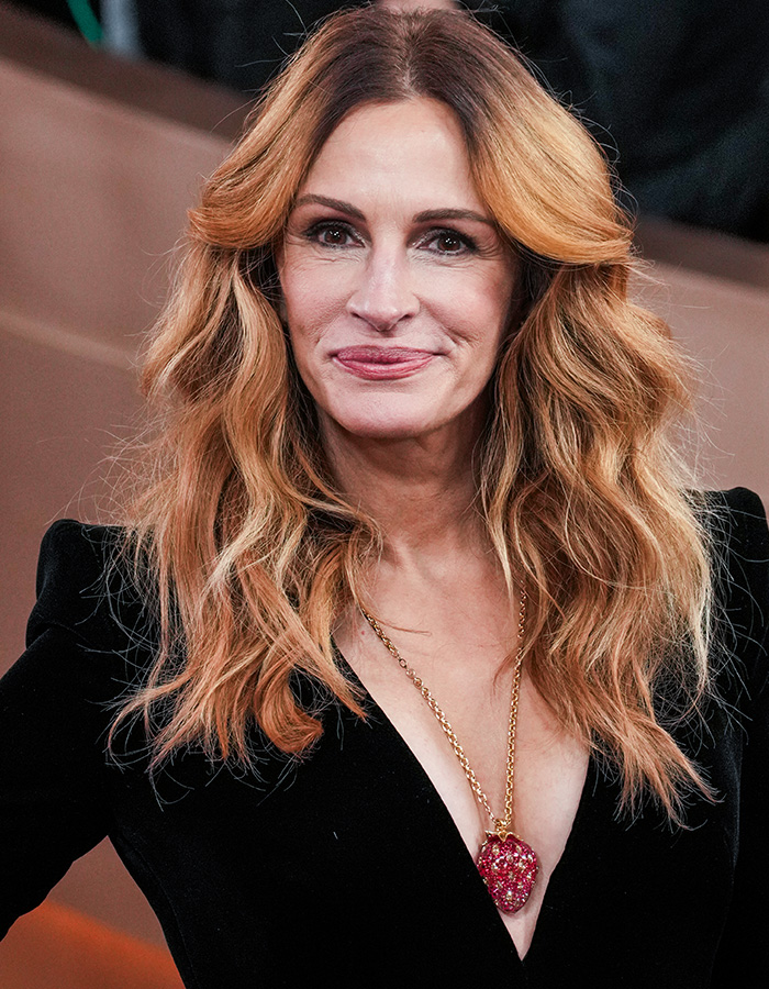 Woman with golden waves hairstyle and glowing skin wearing a black outfit and statement necklace at an event.