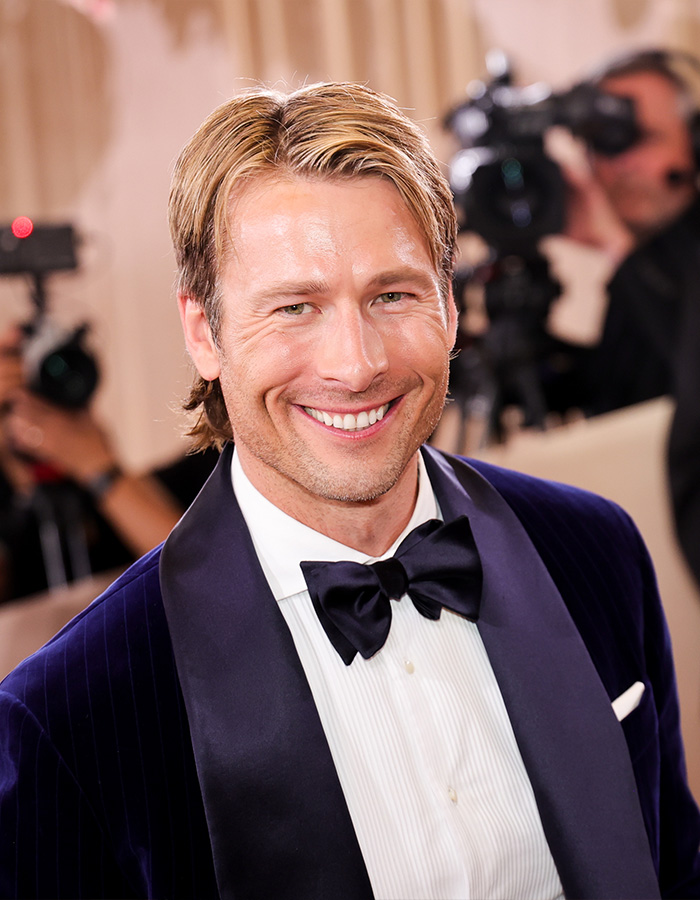 Man in a navy velvet tuxedo smiling at an event, showcasing a glowing complexion without filler or botox.