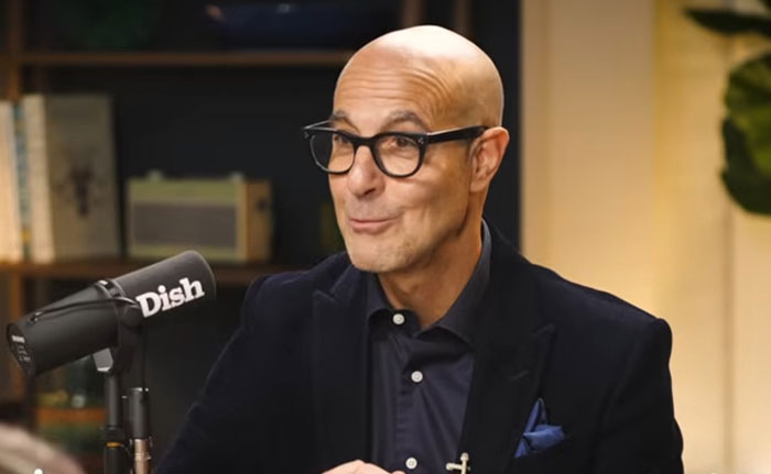 Man wearing glasses and a dark blazer speaking into a Dish microphone about celebrity infidelity scandals in a studio setting