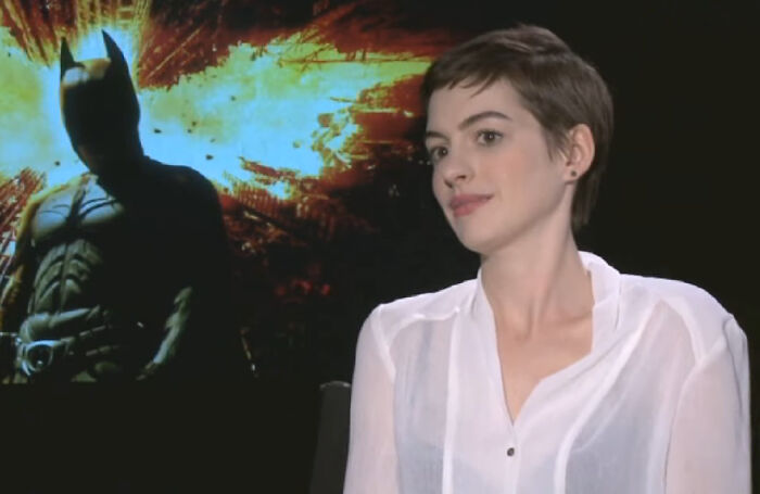 Actress in a white blouse sitting in an interview setting with a Batman poster behind, showing celeb responses.
