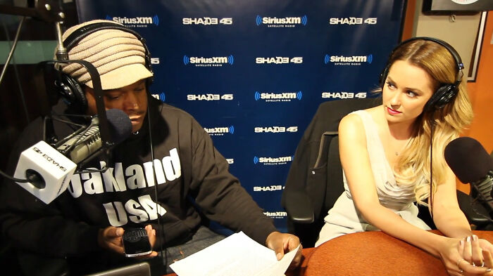 Two celebrities wearing headphones during a radio interview, showing savage responses to annoying interviewer questions.