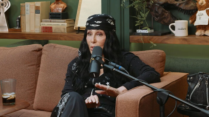 Celebrity wearing black outfit and bandana speaking into microphone during interview with savage responses to questions.