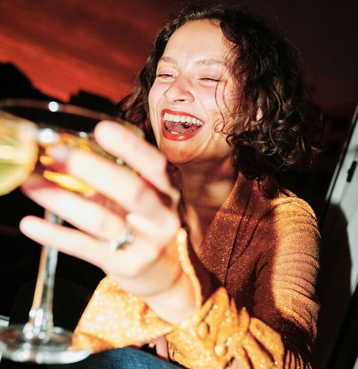 Woman laughing and holding a drink, illustrating actions sparking a double-standard debate about gender behavior. Woman laughing and holding a drink, illustrating actions sparking a double-standard debate about gender behavior.