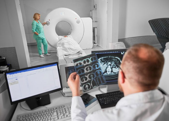 Radiologist reviewing CT images while patient undergoes scan, technician by CT machine — illustrating health signs detection